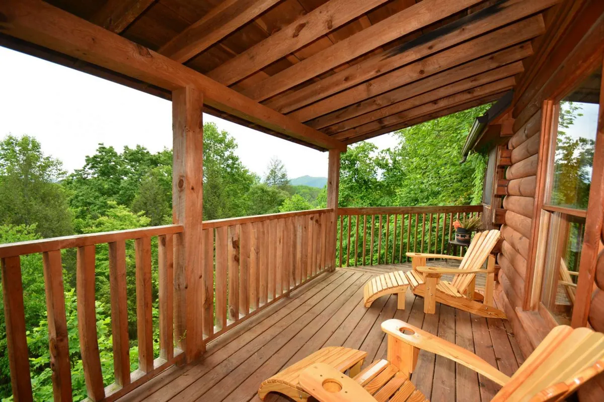 An exterior shot of a spacious wooden deck furnished with classic rocking chairs, surrounded by lush greenery. The setting is peaceful, ideal for relaxing and taking in the natural mountain environment, with plenty of room for gatherings or quiet contemplation.