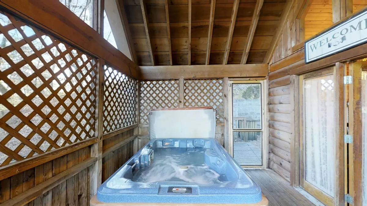 This interior image presents a welcoming hot tub area framed by wooden beams and lattice walls, offering both privacy and rustic charm. The inviting hot tub is the focal point, evoking relaxation and intimate moments, with the promise of soaking together while enjoying the view or starry skies.