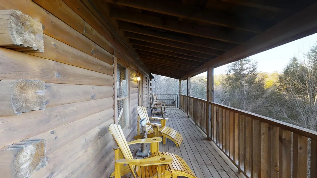 This exterior image showcases a wooden deck outfitted with inviting rocking chairs, surrounded by lush natural scenery. The tranquil atmosphere and views of the landscape create a perfect ambiance for couples to relax, sip coffee, or stargaze in the serene Smoky Mountain setting.