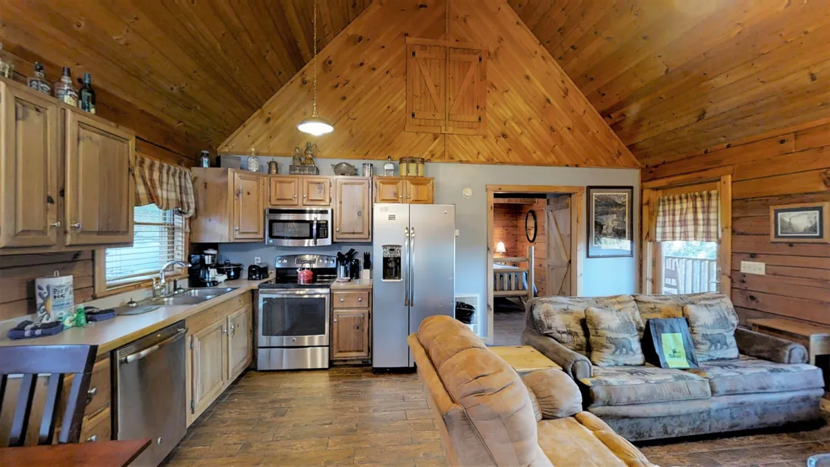 A cozy kitchen scene with modern appliances, wooden ceiling, comfortable sofa, and wood cabinetry. The open-plan design allows easy movement between the kitchen and living area, illustrating how the chef can remain part of the conversation.
