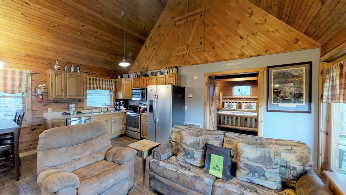 This image showcases a warm, inviting open-plan living space with visible wooden beams, comfortable seating, a kitchen area for family meal prep, and decorative artwork. The arrangement suggests a welcoming environment ideal for socializing and relaxing after a day of outdoor adventure.