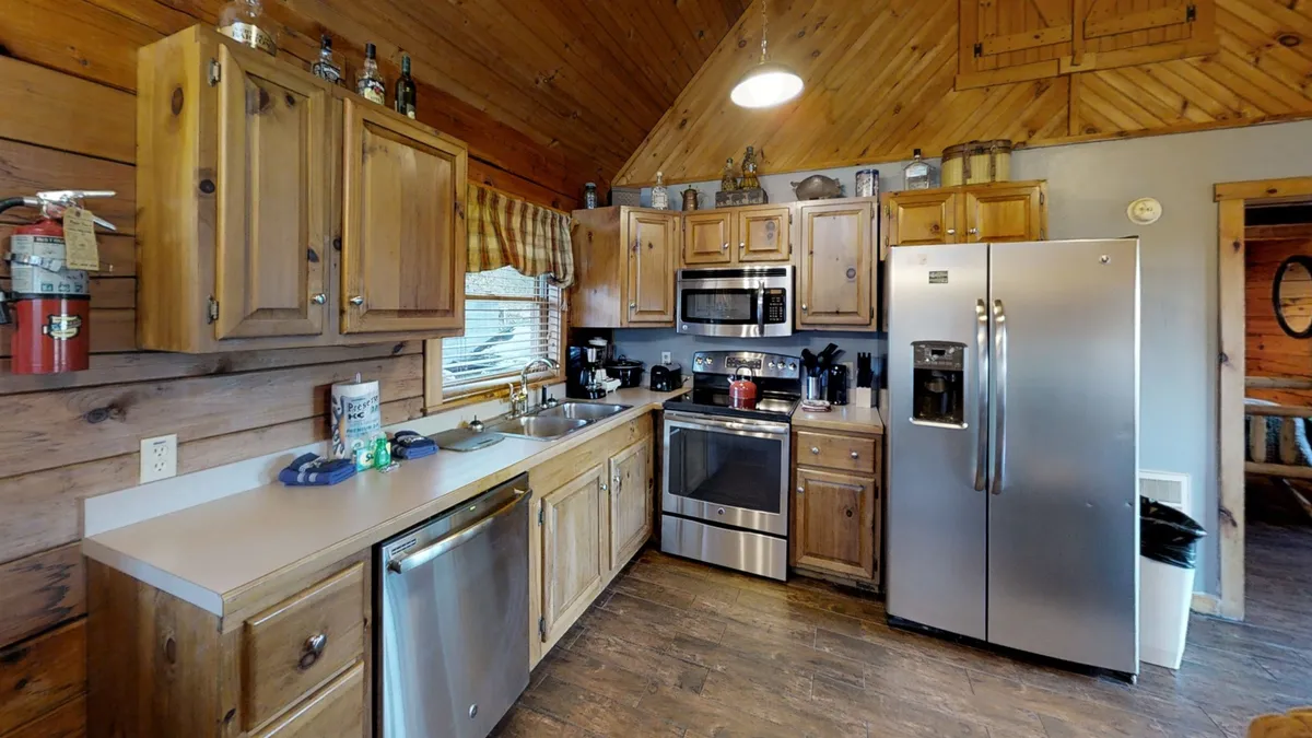 A view of the kitchen featuring warm wooden cabinetry, sleek stainless steel appliances, and a window that lets in natural light. The countertops are spacious and uncluttered, with cookware and utensils visible, conveying a ready-to-use, fully-equipped space.