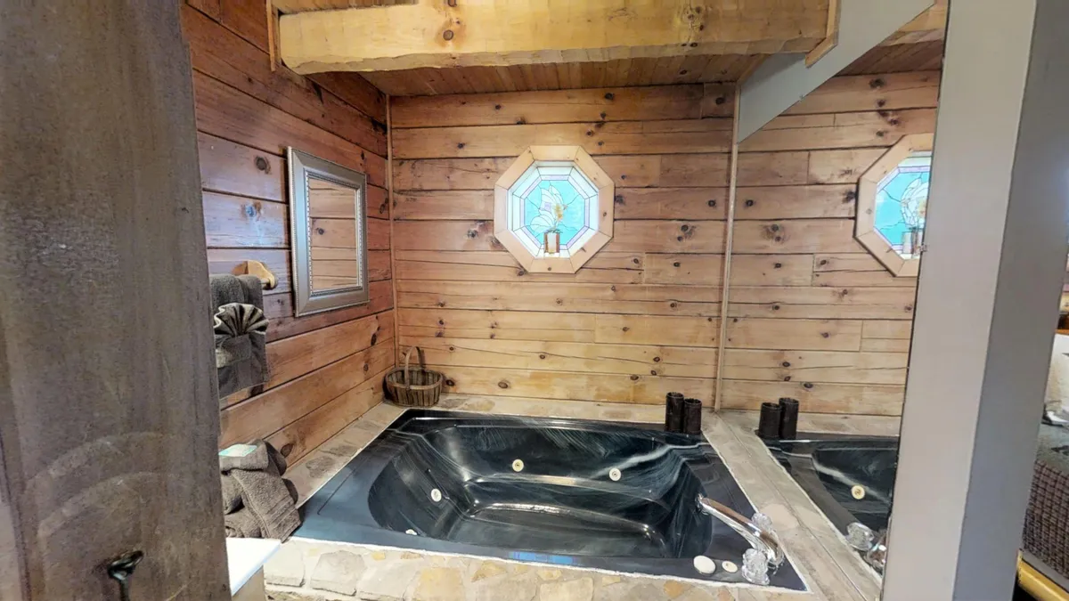 A tranquil interior scene featuring a black hot tub set against wooden walls, with an octagonal stained glass window allowing in warm light. The space exudes relaxation and a spa-like ambiance, perfect for unwinding after a day of mountain adventures.