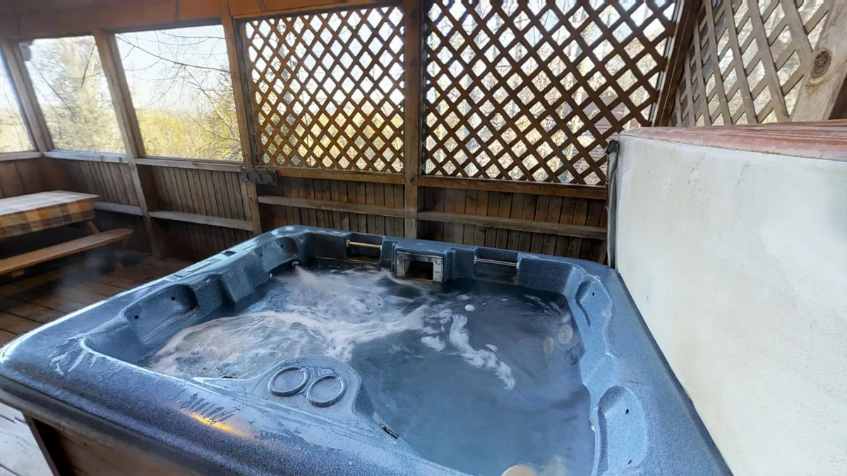 This image features a cozy hot tub with wooden lattice surroundings and built-in bench seating. Guests can relax in the tub or enjoy a morning coffee while taking in unobstructed views of the outdoors, perfect for socializing or winding down after a day of adventure.
