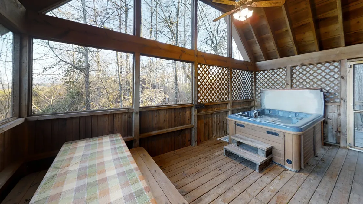 This image showcases a serene wooden hot tub area surrounded by screened windows, providing relaxing views of nature. The wooden seating area invites guests to linger and socialize while enjoying the fresh mountain air, and the setup encourages guests to unwind and stargaze directly from the hot tub.